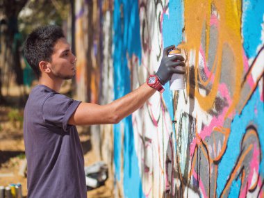 Yakışıklı yetenekli genç çocuk kentsel sokak duvara aerosol sprey ile renkli bir graffiti yapmak. Sinema tonedshot. Yaratıcı sanat. Yan görünüm