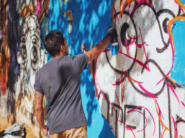 Yaratıcı sanat - genç çocuk sokak duvarına sprey spreyle renkli soyut süsleme grafitisi çiziyor. Arka plan, genel plan