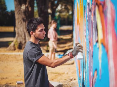 Yakışıklı yetenekli genç çocuk kentsel sokak duvara aerosol sprey ile renkli bir graffiti yapmak. Sinema tonedshot. Yaratıcı sanat. Yan görünüm