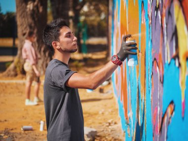 Yakışıklı yetenekli genç çocuk kentsel sokak duvara aerosol sprey ile renkli bir graffiti yapmak. Sinema tonedshot. Yaratıcı sanat. Yan görünüm
