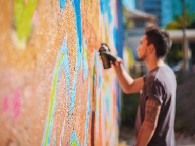 Yakışıklı yetenekli genç çocuk kentsel sokak duvara aerosol sprey ile renkli bir graffiti yapmak. Sinema tonedshot. Yaratıcı sanat. Yan görünüm