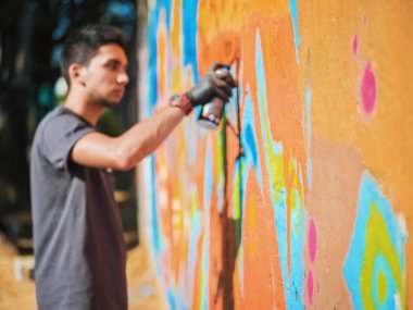 Yakışıklı yetenekli genç çocuk kentsel sokak duvara aerosol sprey ile renkli bir graffiti yapmak. Sinema tonedshot. Yaratıcı sanat. Yan görünüm