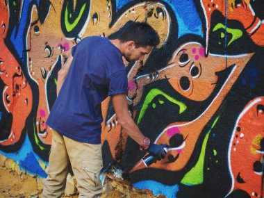 Yakışıklı yetenekli genç çocuk kentsel sokak duvara aerosol sprey ile renkli bir graffiti yapmak. Sinema tonedshot. Yaratıcı sanat. Yan görünüm