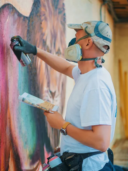 Graffiti Artist Painting On The Street Wall. Man with aerosol spray bottle near the wall. Young talented guy in protective mask drawing colorful lion. — Stock Photo, Image