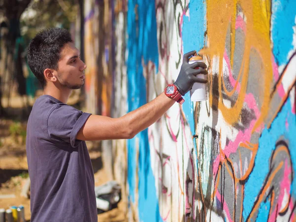 Handsome Talented Young Boy making a colorful graffiti with aerosol spray on urban street wall. Cinematic tonedshot. Creative art. Side view — Stock Photo, Image
