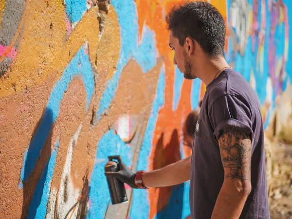 Yakışıklı yetenekli genç çocuk kentsel sokak duvara aerosol sprey ile renkli bir graffiti yapmak. Sinema tonedshot. Yaratıcı sanat. Yan görünüm