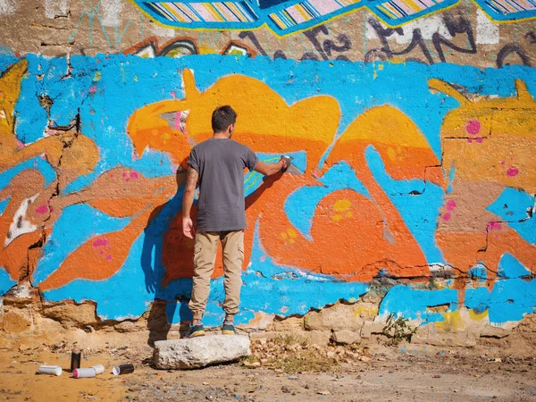 Creative art - teenage boy painting colorful abstract ornament graffiti on street wall with aerosol spray. Back view, overall plan — Stock Photo, Image