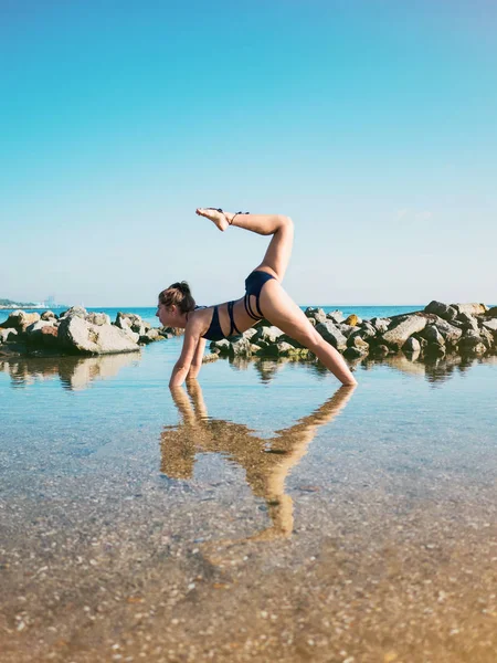 Mulher caucasiana jovem em maiô praticando ioga em água do mar, lago ou rio. Belo reflexo. Asanas complexas, equilíbrio. Fitness, esporte, ioga e conceito de estilo de vida saudável . — Fotografia de Stock