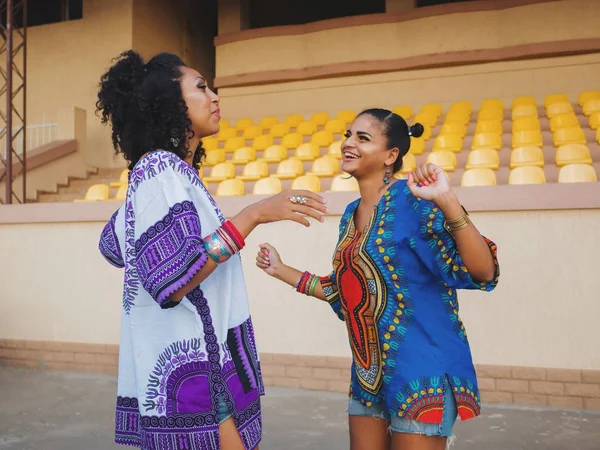 Dwa szczęśliwy piękne kobiety afro-amerykański znajomych stojąc na zewnątrz. Młody mieszane rasy dziewczyny komunikuje się noszenie odzież kolorowe, cieszy się na spotkanie i roześmiany — Zdjęcie stockowe