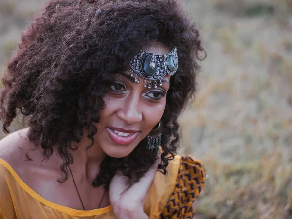 カラフルな黄色の伝統的なドレスと笑顔とカメラに近いダンスのおでこに銀冠若いアフリカ系アメリカ人のジプシーの女性の肖像画。巻き髪とセクシーなファッションの女の子 — ストック写真