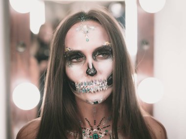 Korkunç genç kız soyunma odasında yaratıcı Cadılar Bayramı savaş-boya ile. Göz alıcı kafatası ile rhinestones ve payetler portresi. Kutlama için profesyonel makyaj.