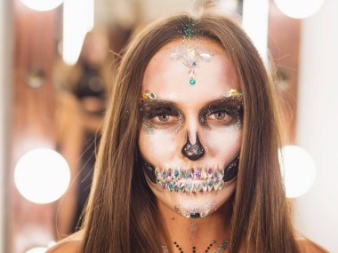 Korkunç genç kız soyunma odasında yaratıcı Cadılar Bayramı savaş-boya ile. Göz alıcı kafatası ile rhinestones ve payetler portresi. Kutlama için profesyonel makyaj.