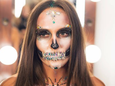 Korkunç genç kız soyunma odasında yaratıcı Cadılar Bayramı savaş-boya ile. Göz alıcı kafatası ile rhinestones ve payetler portresi. Kutlama için profesyonel makyaj.