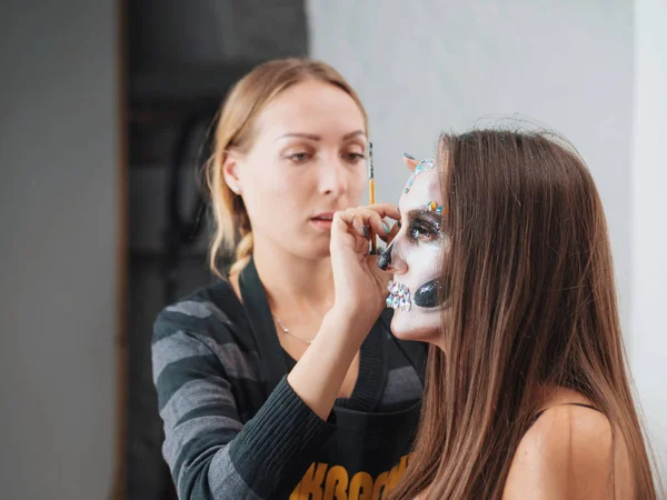 Make-up artist make-up membuat gadis halloween make up di studio.Halloween wajah art.Woman berlaku pada greasepaint profesional di wajah gadis-Perang cat dengan darah, bekas luka dan luka . — Stok Foto