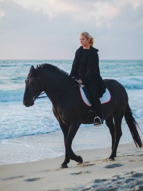 siyah ata denizde plaj oturan kadın. Güzel kadın zevk gündoğumu sabah okyanus su yakın siyah giysili.