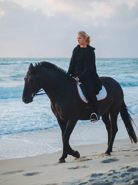 siyah ata denizde plaj oturan kadın. Güzel kadın zevk gündoğumu sabah okyanus su yakın siyah giysili.