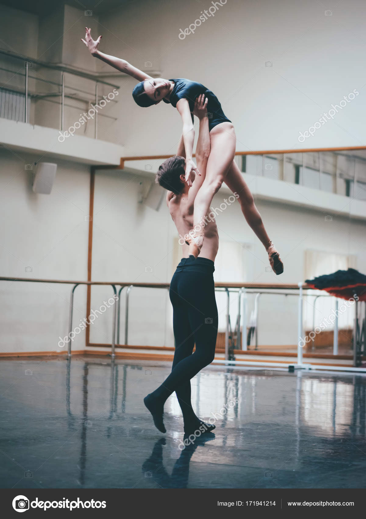 Jongeman oefenen in klassiek ballet met jonge mooie vrouw in zwarte kleding in de sportschool of ballet hall. Paar springen dansende sensuele dans. Minimalisme interieur Stockfoto kohanova1991 1719412...