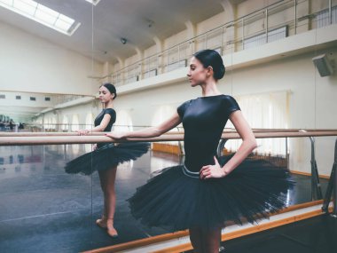 Siyah tutu ve pointe balerin bale salonunda barre üzerinde uzanır. Yakın duran kadın bar ve ayna, perfomance için hazırlanıyor.
