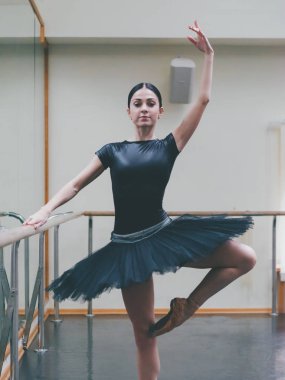 Siyah tutu ve pointe balerin bale salonunda barre üzerinde uzanır. Yakın duran kadın bar ve ayna, perfomance için hazırlanıyor.