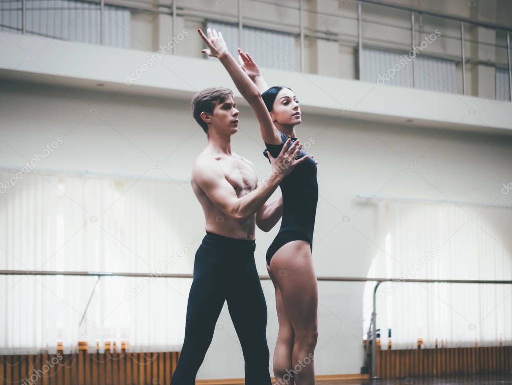 Young man practicing in classical ballet with young beautiful woman in black clothing in the gym or ballet hall. Couple jumping dancing sensual dance. Minimalism interior,