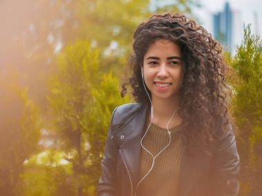 Siyah kıvırcık uzun saç kulaklık ve smartphone ya da ıssız bir sonbahar sokak üzerinde oyuncu ile müzik dinleme genç ve güzel latin kız. Kadın zevk an.