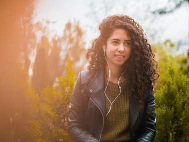 Siyah kıvırcık uzun saç kulaklık ve smartphone ya da ıssız bir sonbahar sokak üzerinde oyuncu ile müzik dinleme genç ve güzel latin kız. Kadın zevk an.