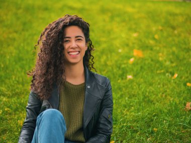 Güzel esmer uzun kıvırcık saç İspanyol kız portre portre sonbaharda yeşil Park'ta açık havada. Kadın güzel görünüyor, gülüyor, gülüyor ve ürkek flört ediyor