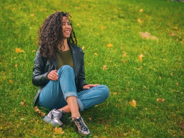 Güzel esmer uzun kıvırcık saç İspanyol kız portre portre sonbaharda yeşil Park'ta açık havada. Kadın güzel görünüyor, gülüyor, gülüyor ve ürkek flört ediyor