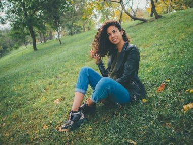 Güzel esmer uzun kıvırcık saç İspanyol kız portre portre sonbaharda yeşil Park'ta açık havada. Kadın güzel görünüyor, gülüyor, gülüyor ve ürkek flört ediyor