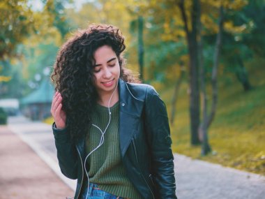 Kıvırcık saçlı kulaklık müzik dinlerken mutlu Afrikalı genç bayan. Dans ritim ve melodi sonbahar park boyunca şarkı İspanyol hippi kız.