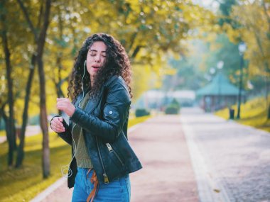 Kıvırcık saçlı kulaklık müzik dinlerken mutlu Afrikalı genç bayan. Dans ritim ve melodi sonbahar park boyunca şarkı İspanyol hippi kız.