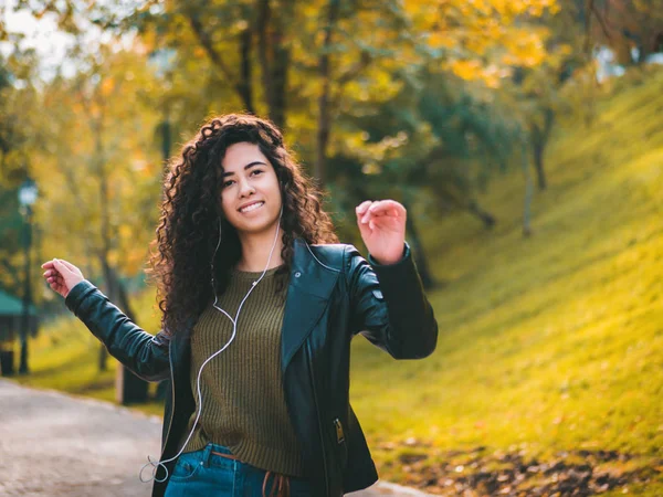 Kıvırcık saçlı kulaklık müzik dinlerken mutlu Afrikalı genç bayan. Dans ritim ve melodi sonbahar park boyunca şarkı İspanyol hippi kız.