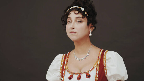 Beautiful woman standing in old historical 18th century royal dress on black background in studio. Look of Marie Antoinette on ball. Details of costume, treasure jewelry.