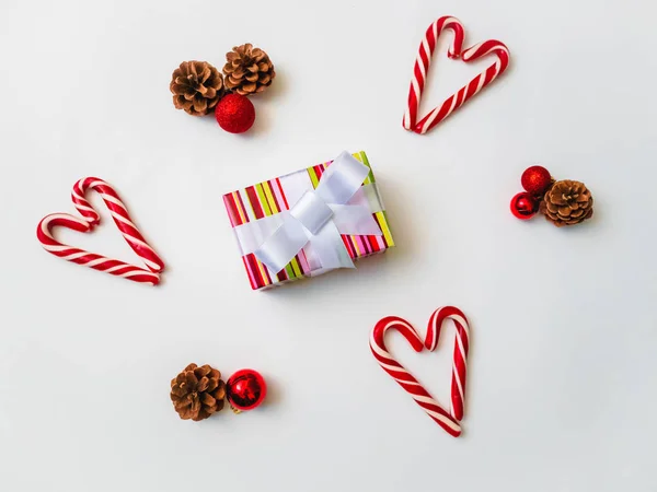 Gioioso sfondo natalizio. Bella scatola regalo, tradizionali lecca-lecca di canna da zucchero, coni. Preparazione per il concetto di vacanze invernali, vista dall'alto — Foto Stock
