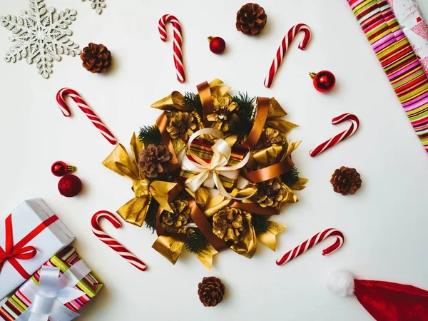 Vista dall'alto Composizione natalizia. Sfondo natalizio, ghirlanda di pino, scatole regalo con nastro di tessuto rosso, cappello di Babbo Natale, lecca-lecca di canna, coni e fiocchi di neve — Foto Stock