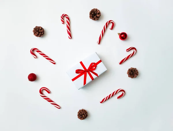Fondo de Navidad alegre. Hermosa caja de regalo, piruletas tradicionales de bastón de caramelo, conos y juguetes de bolas de árbol. Preparación para el concepto de vacaciones de invierno, vista superior — Foto de Stock