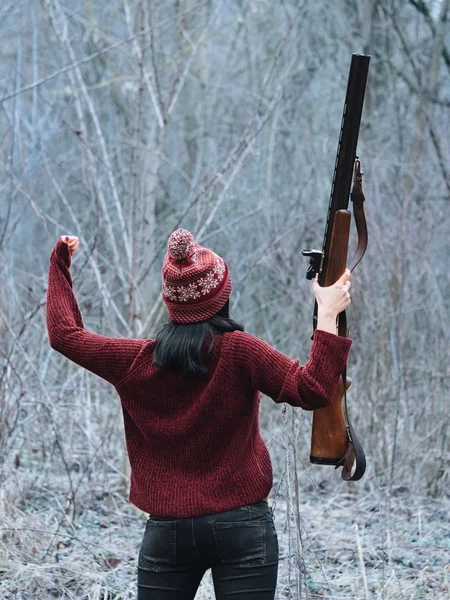 Mulher caçadora em roupas quentes da Borgonha com arma. Menina caçando na floresta e se alegra com sua vitória, levantando rifle depois de disparar . — Fotografia de Stock