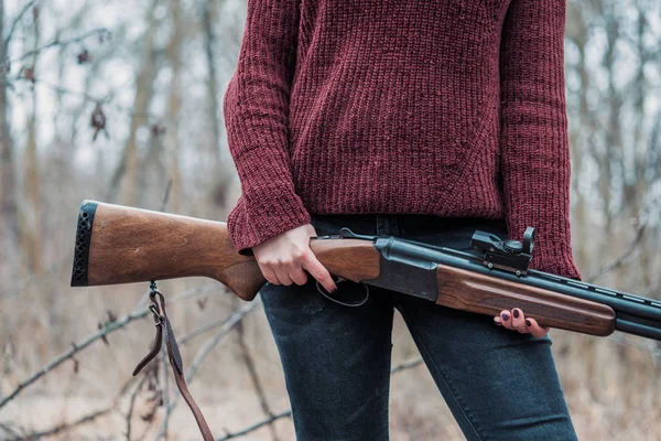 Cacciatrice in abiti caldi bordeaux con pistola. Ragazza a caccia nella foresta tenendo il fucile da vicino . — Foto Stock
