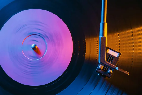 Movie of retro-styled record player spinning vinyl black record. Cinemagraph. Side view. Beautiful neon night colors.