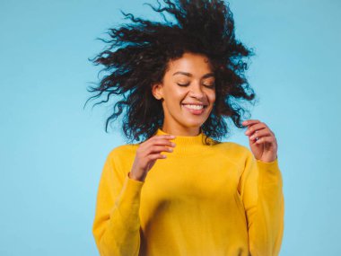 karışık ırk siyah kadın portre dans mavi arka plan üzerinde büyük afro kıvırcık saçlı ve havada uçan saç modeli ile