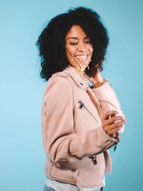 Köpüklü Bengal ateşi mavi zemin üzerine Afrika kökenli Amerikalı kadının elinde. Noel tatil kavramı. Genç güzel kız kutluyor, gülümseyen, vaktinizi afro saç modeli ile