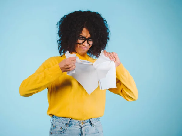 Breaking contract. Furious young african american woman with afro hairstyle tearing up paper on blue background.