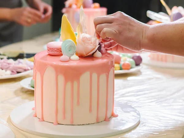 Oigenkännliga kvinna dekorera moussen glasyr tårta med ros, macarons, händerna detalj, fokus på kakan. DIY, sekvens, steg för steg, en del av serien. — Stockfoto