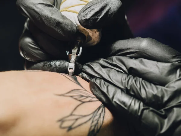 Tattoo artist at work. Woman in black latex glove tattooing a young mans hand with colorful picture in studio. Macro. — Stock Photo, Image