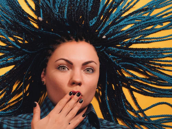 Surprised young woman with long blue kanekalon african braids shouting over yellow background. Girl looking at camera with open mouth. — Stock Photo, Image