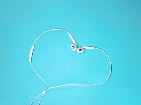 Earphone putih hati berbentuk pada latar belakang biru. Konsep musik. Salin ruang — Stok Foto