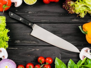 Taze çiftlik sebze, sarı kırmızı biber biber, fesleğen, domates, mantar, kırmızı soğan, limon, marul ile mutfak siyah çerçeve arka plan. Gıda üstten görünüm. Büyük şef bıçak orta