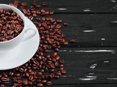 Beyaz porselen kahve fincanı ve siyah eski püskü ahşap zemin üzerine kavrulmuş fasulye. Üstten Görünüm. Kopya alanı.