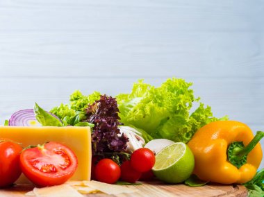 İştah açıcı natürmort. Taze kiraz domates, marul yaprakları, mantar, yeşil fesleğen, ahşap tahta üzerinde peynir. Beyaz duvar izole sebze.