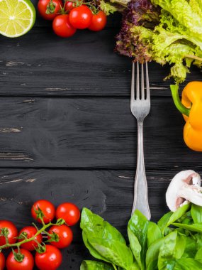 Taze sebze, sarı kırmızı biber biber, fesleğen, domates, mantar, kırmızı soğan, limon, marul ile mutfak siyah ahşap çerçeve arka plan. Gıda üstten görünüm. Orta çatal.